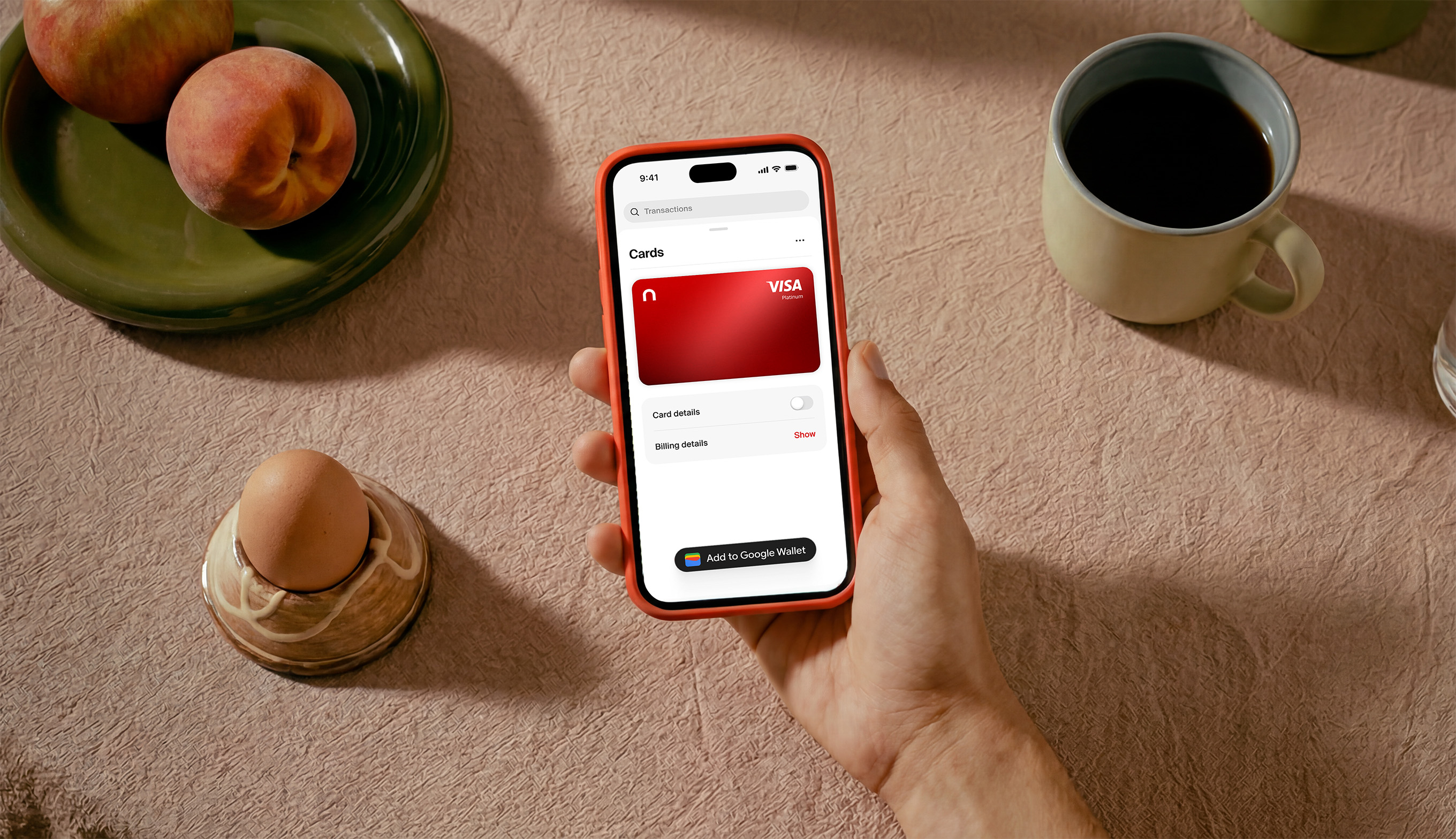 Hand holding a phone showing the nsave app with a red nsave Visa card on a breakfast table