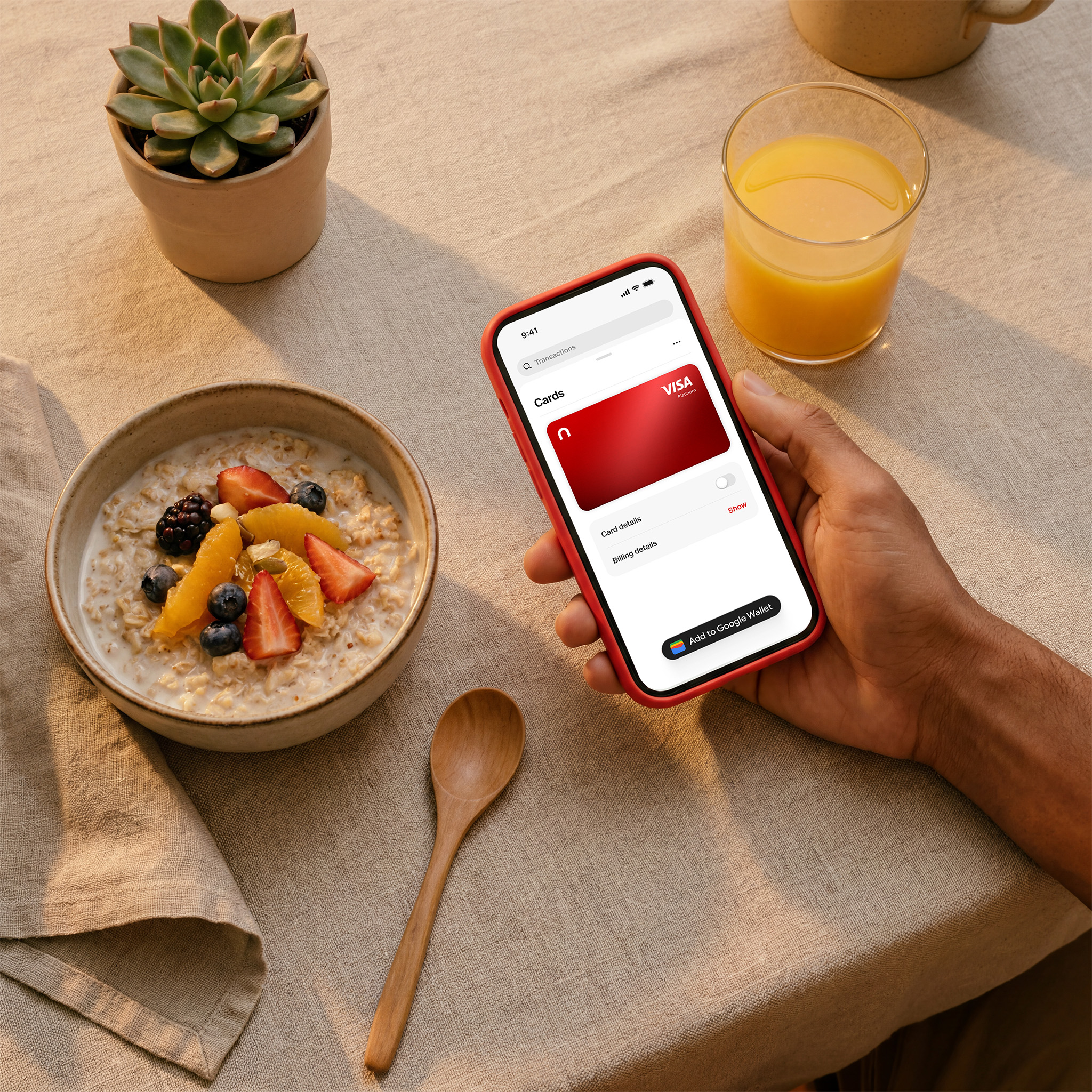 Person holding a phone displaying the nsave Visa card beside a breakfast bowl and orange juice